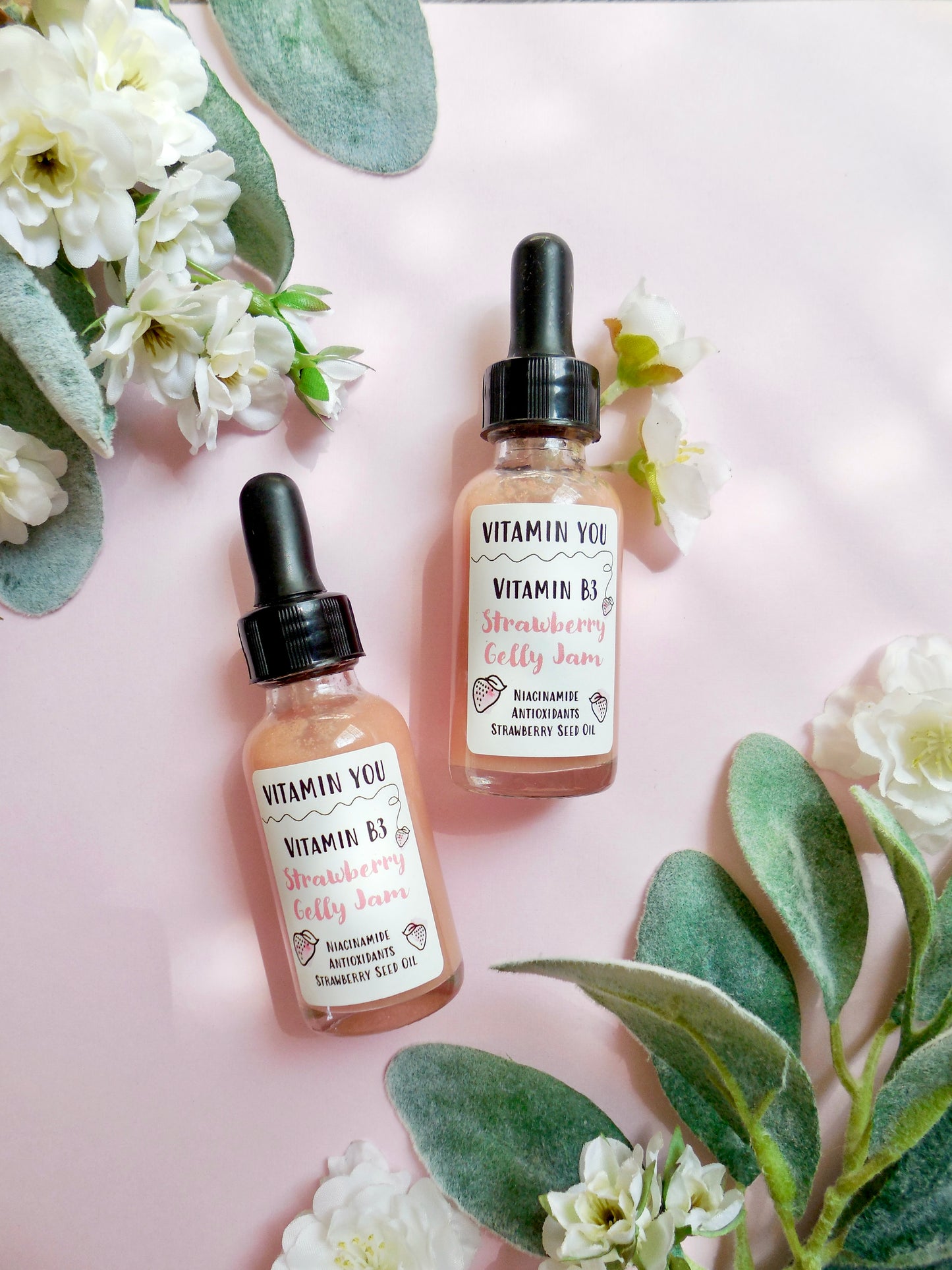 Pink shimmery strawberry niacinamide facial gel serums on a pink background surrounded by flowers