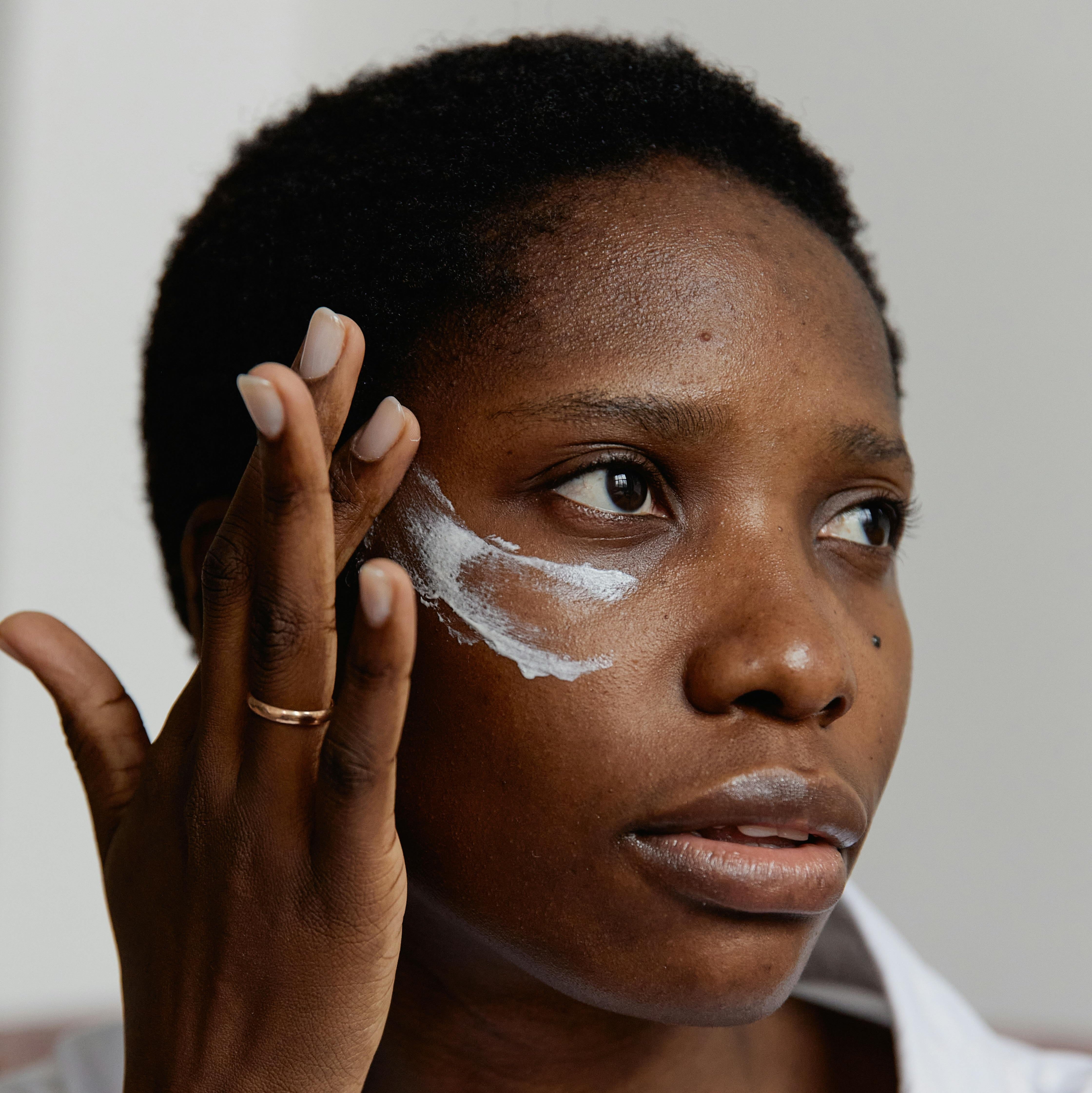 Woman with dry skin applying face cream onto cheek.