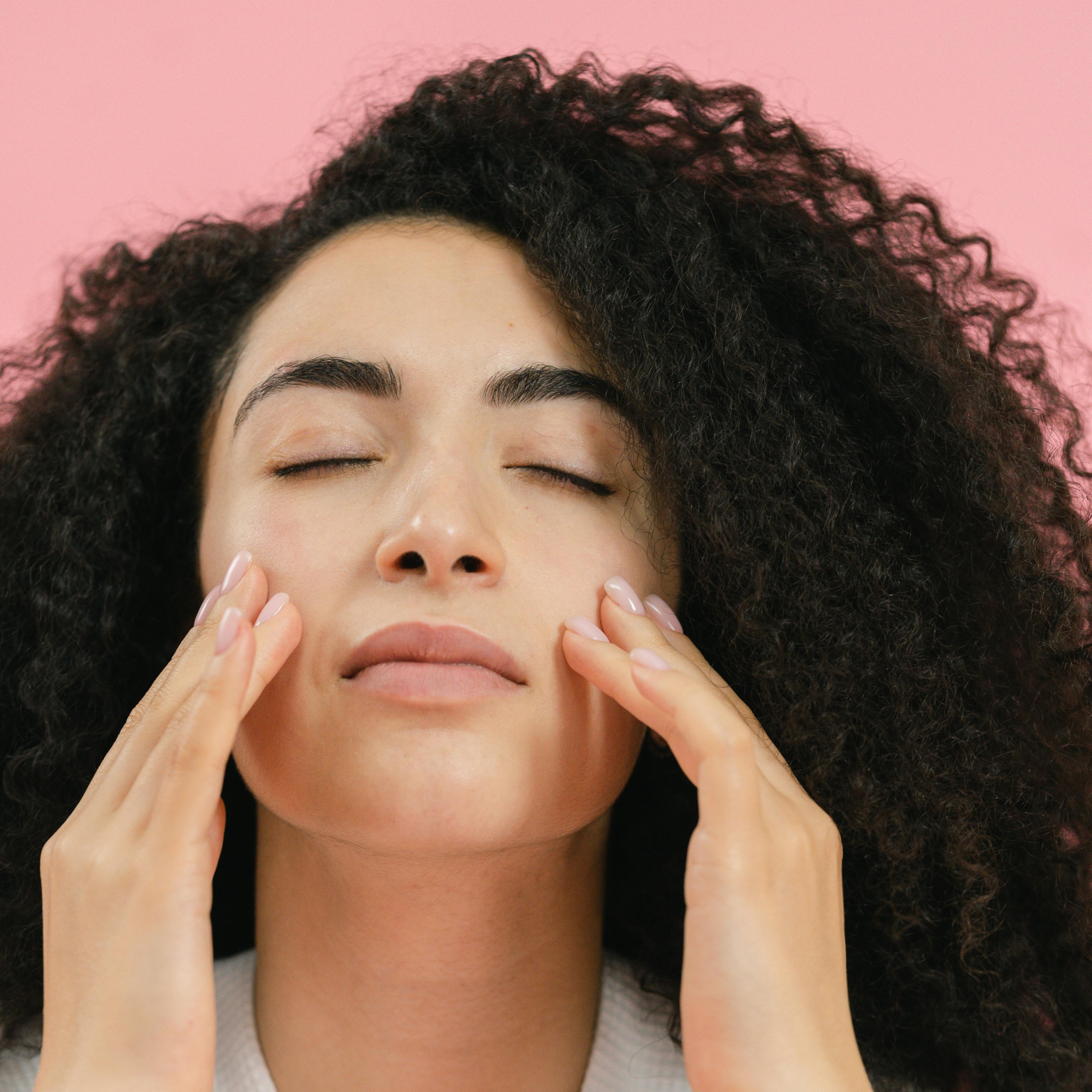 Woman patting skincare into skin with pink background