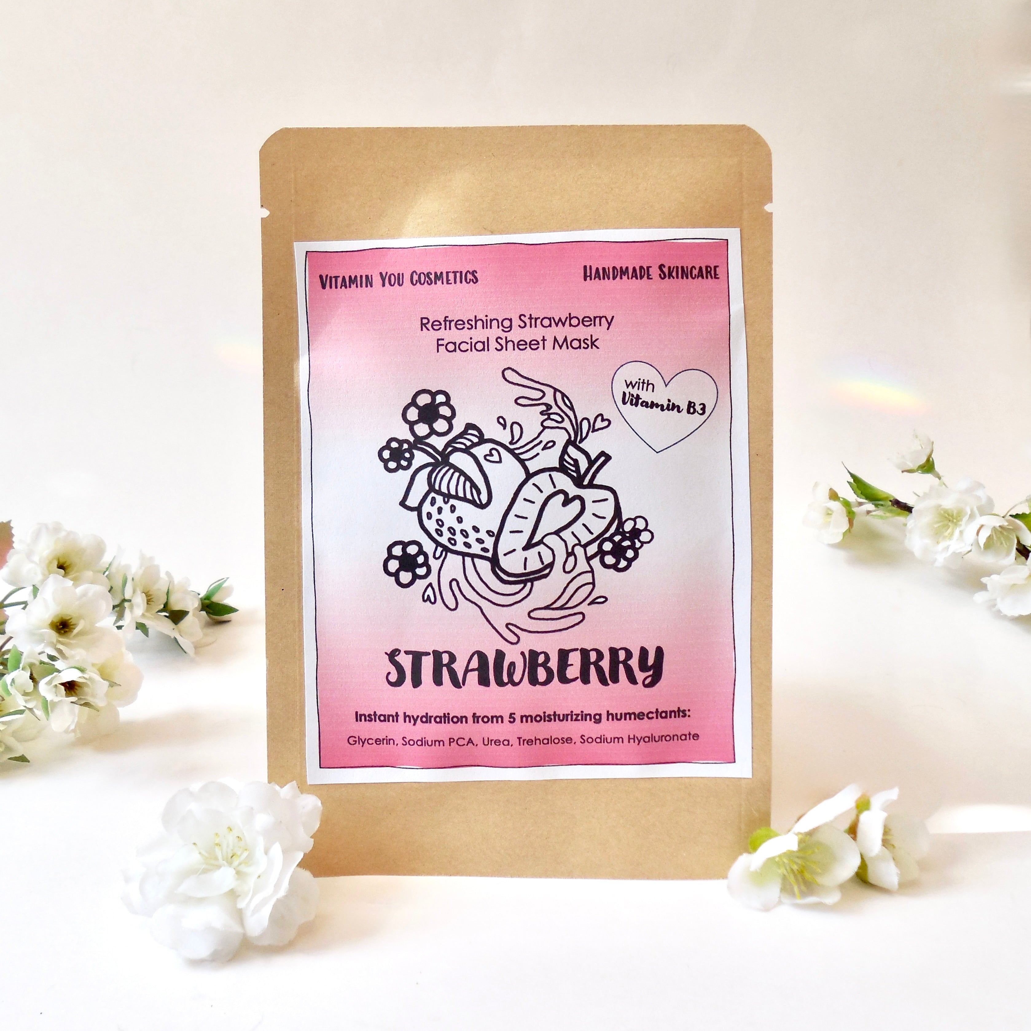A packaged facial sheet mask product with a strawberry theme, displayed alongside decorative flowers.