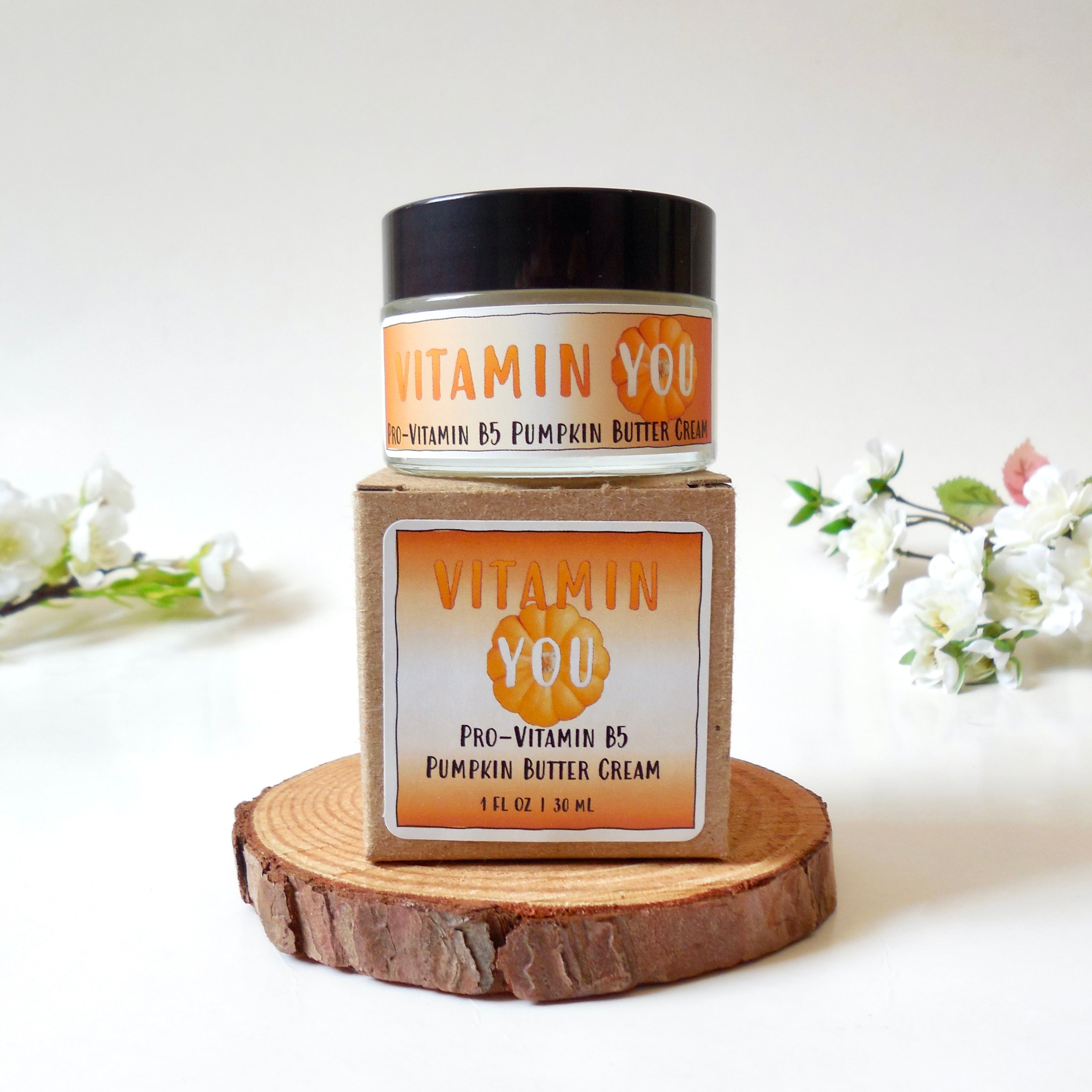 Jar of Vitamin You's Vitamin B5 Pumpkin Butter on display with an orange theme surrounded by white flowers.